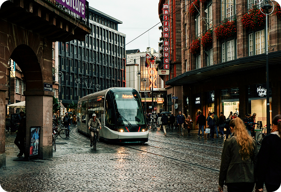 A modern Strasbourg tram navigating a cobblestone city street lined with historic buildings and pedestrians, illustrating local transit options for the Usability Conference Symposium.